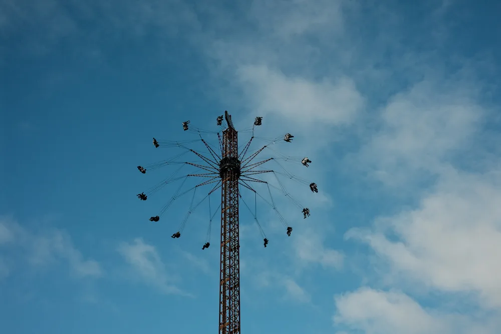 Seats on a swing ride circling a tall tower high against the sky