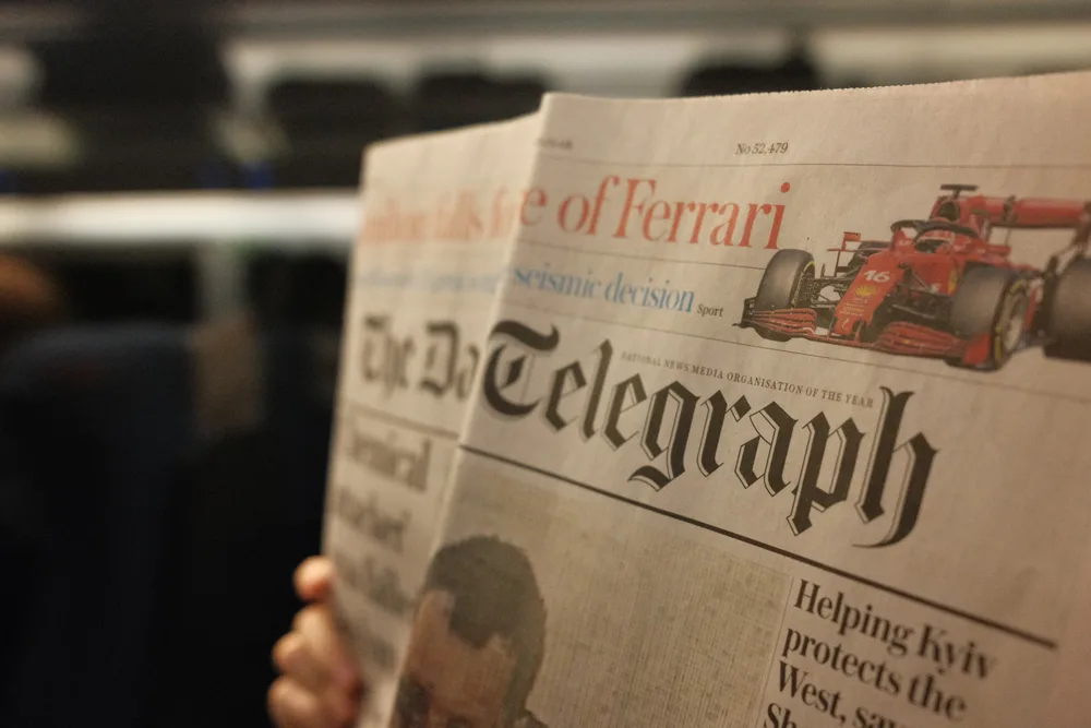 A passenger holding an open copy of The Telegraph inside a train carriage