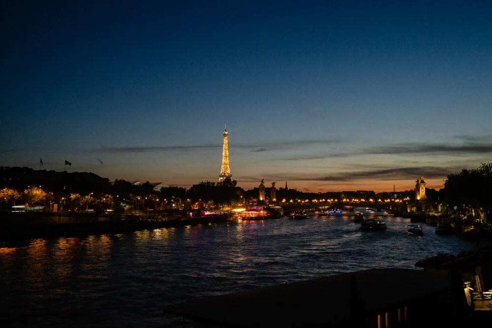 The illuminated Eiffel Tower above the Seine at dusk, with lights reflected in the water